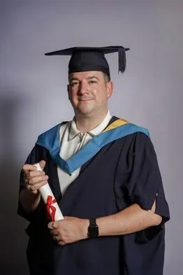 Matt wearing graduation robes and holding his degree certificate